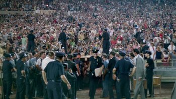 Movie still from “The Beatles: Eight Days a Week - The Touring Years” (2016), directed by Ron Howard – A large crowd of people in a stadium with police standing around them; Extreme Wide shot, High angle