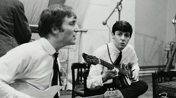 Movie still from “The Beatles: Eight Days a Week - The Touring Years” (2016), directed by Ron Howard – Two men sitting in a chair playing a guitar; Close Up shot, Low angle