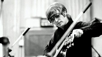 Movie still from “The Beatles: Eight Days a Week - The Touring Years” (2016), directed by Ron Howard – A man in sunglasses playing a guitar in front of a microphone; Close Up shot, Low angle