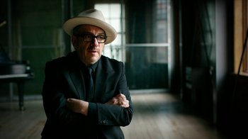 Movie still from “The Beatles: Eight Days a Week - The Touring Years” (2016), directed by Ron Howard – A man wearing a hat and glasses standing in a room; Close Up shot, Low angle