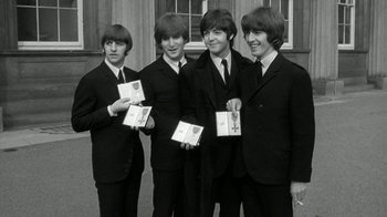 Movie still from “The Beatles: Eight Days a Week - The Touring Years” (2016), directed by Ron Howard – A black and white photo of four young men holding awards; Medium shot, High angle
