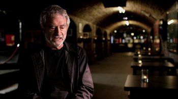 Movie still from “The Beatles: Eight Days a Week - The Touring Years” (2016), directed by Ron Howard – An older man sitting on a bench at night; Medium shot, Low angle