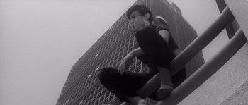 A man sitting on top of a building in front of a tall building