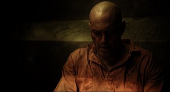 A bald man in a orange shirt is looking down
