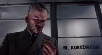 Movie still from “Brazil” (1985), directed by Terry Gilliam – A man in a suit and tie holding a piece of food; Close Up shot, Low angle