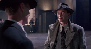 Movie still from “Brazil” (1985), directed by Terry Gilliam – A man wearing a hat and a suit talking to another man wearing a hat; Medium shot, Over the shoulder angle