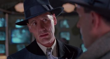 Movie still from “Brazil” (1985), directed by Terry Gilliam – A person wearing a suit and a hat; Close Up shot, Over the shoulder angle