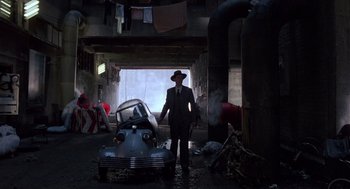 Movie still from “Brazil” (1985), directed by Terry Gilliam – A man standing next to an old car in a garage; Wide shot, Low angle