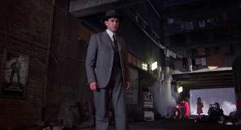 Movie still from “Brazil” (1985), directed by Terry Gilliam – A man in a suit and hat standing in front of a building; Wide shot, Low angle