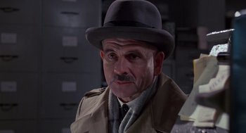 Movie still from “Brazil” (1985), directed by Terry Gilliam – An older man wearing a hat and a trench coat; Close Up shot, Low angle