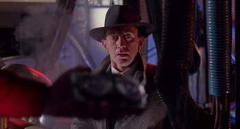 Movie still from “Brazil” (1985), directed by Terry Gilliam – A man wearing a hat and holding a camera in his hand; Close Up shot, Over the shoulder angle