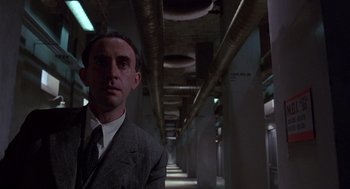 Movie still from “Brazil” (1985), directed by Terry Gilliam – A man wearing a suit and tie in a dark room; Close Up shot, Low angle
