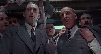 Movie still from “Brazil” (1985), directed by Terry Gilliam – A group of men standing next to each other in suits; Medium shot, Low angle