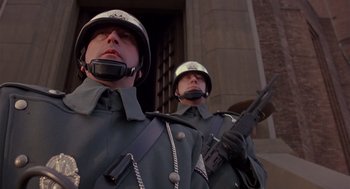 Movie still from “Brazil” (1985), directed by Terry Gilliam – A couple of men standing next to each other holding guns; Close Up shot, Low angle