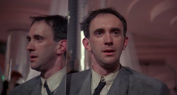 Movie still from “Brazil” (1985), directed by Terry Gilliam – A man wearing a suit and tie looking at his reflection in a mirror; Close Up shot, Low angle