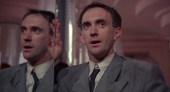 Movie still from “Brazil” (1985), directed by Terry Gilliam – A man wearing a suit and tie looking at his reflection in a mirror; Close Up shot, Low angle