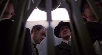 Movie still from “Brazil” (1985), directed by Terry Gilliam – Two men in suits and a hat are looking at each other; Close Up shot, Low angle