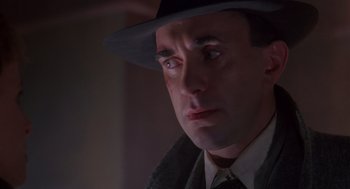 Movie still from “Brazil” (1985), directed by Terry Gilliam – A person wearing a suit and a hat; Close Up shot, Low angle