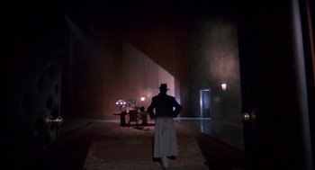 Movie still from “Brazil” (1985), directed by Terry Gilliam – A man standing in front of a table in a dark room; Wide shot, Low angle