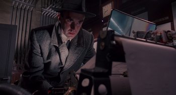 Movie still from “Brazil” (1985), directed by Terry Gilliam – A man wearing a hat and a suit looking at a camera; Medium shot, Low angle