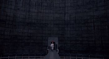 Movie still from “Brazil” (1985), directed by Terry Gilliam – A man standing in front of a large wall; Extreme Wide shot, Low angle