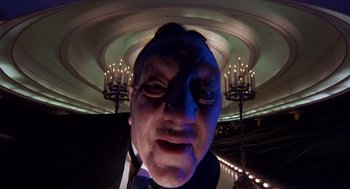 Movie still from “Brazil” (1985), directed by Terry Gilliam – A man in a suit and tie with a blue mask on his face; Close Up shot, Low angle