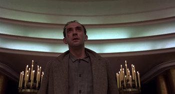Movie still from “Brazil” (1985), directed by Terry Gilliam – A man standing in front of candles in a room; Medium shot, Low angle