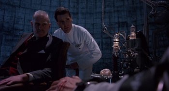 Movie still from “Brazil” (1985), directed by Terry Gilliam – Two men are sitting at a table and one of them is holding a fake head; Medium shot, Low angle
