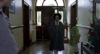 Movie still from “Breakfast on Pluto” (2005), directed by Neil Jordan – A woman in a coat and tie in a room; Wide shot, Low angle