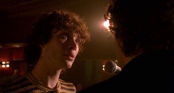 Movie still from “Breakfast on Pluto” (2005), directed by Neil Jordan – A man with curly red hair talking to another man in front of a microphone; Close Up shot, Over the shoulder angle