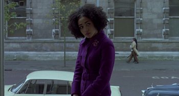 Movie still from “Breakfast on Pluto” (2005), directed by Neil Jordan – A woman in a purple coat standing on the side of the road; Medium shot, Low angle