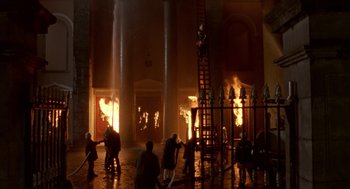 Movie still from “Breakfast on Pluto” (2005), directed by Neil Jordan – A group of people standing next to a building on fire; Extreme Wide shot, High angle