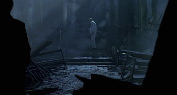 Movie still from “Breakfast on Pluto” (2005), directed by Neil Jordan – A man standing in a dark room next to a pile of rubble; Wide shot, Low angle
