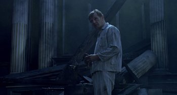 Movie still from “Breakfast on Pluto” (2005), directed by Neil Jordan – A man in pajamas standing next to a fire damaged building; Medium shot, Low angle