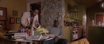 Movie still from “Breakin' All the Rules” (2004), directed by Daniel Taplitz – A man sitting at a table with papers on the table and a woman standing at the table; Medium shot, High angle