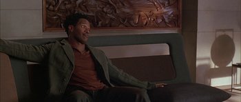 Movie still from “Breakin' All the Rules” (2004), directed by Daniel Taplitz – A man sitting on top of a couch in front of a statue; Medium shot, High angle