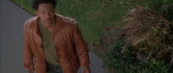 Movie still from “Breakin' All the Rules” (2004), directed by Daniel Taplitz – A man wearing a brown leather jacket standing next to a tree; Medium shot, Overhead angle