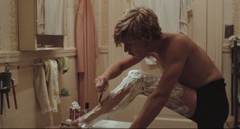 Movie still from “Breaking Away” (1979), directed by Peter Yates – A shirtless man shaving in a bathroom with a toothbrush; Medium shot, Over the shoulder angle