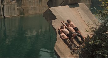 Movie still from “Breaking Away” (1979), directed by Peter Yates – Three men laying on the side of a rock wall; Wide shot, Overhead angle