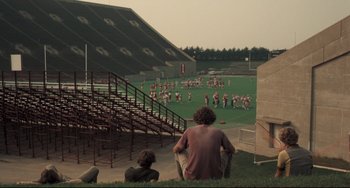 Movie still from “Breaking Away” (1979), directed by Peter Yates – Two people sitting on the bleachers watching a football game; Extreme Wide shot, High angle