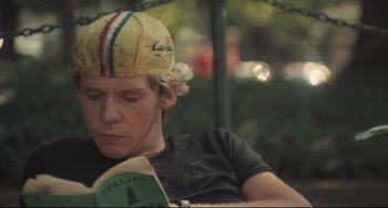 Movie still from “Breaking Away” (1979), directed by Peter Yates – A young man wearing a hat while reading a book; Close Up shot, Over the shoulder angle