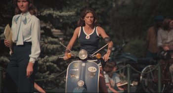 Movie still from “Breaking Away” (1979), directed by Peter Yates – A woman riding on the back of a blue scooter; Wide shot, Low angle