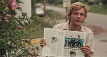 Movie still from “Breaking Away” (1979), directed by Peter Yates – A man is holding a newspaper while standing next to a tree; Close Up shot, Over the shoulder angle