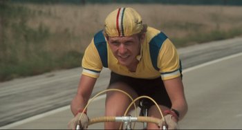 Movie still from “Breaking Away” (1979), directed by Peter Yates – A man riding a bike on a road with a helmet on; Close Up shot, Low angle