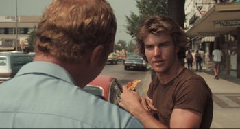 Movie still from “Breaking Away” (1979), directed by Peter Yates – A man holding a slice of pizza in his hand; Close Up shot, Over the shoulder angle