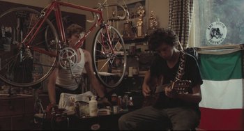 Movie still from “Breaking Away” (1979), directed by Peter Yates – Two young men are playing guitar in a room with bicycles; Wide shot, Low angle