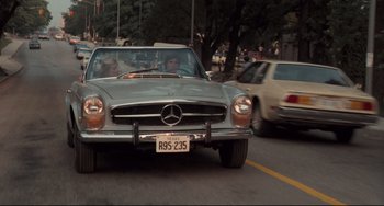 Movie still from “Breaking Away” (1979), directed by Peter Yates – A car driving down a street past a traffic light; Wide shot, Low angle