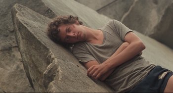 Movie still from “Breaking Away” (1979), directed by Peter Yates – A man laying on the side of a rock wall; Medium shot, High angle