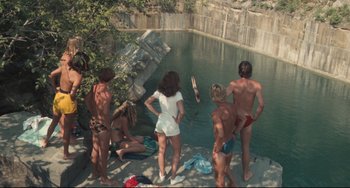 Movie still from “Breaking Away” (1979), directed by Peter Yates – A group of people standing next to a body of water; Extreme Wide shot, High angle