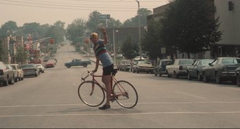 Movie still from “Breaking Away” (1979), directed by Peter Yates – A man riding a bike down the middle of the street; Wide shot, Low angle